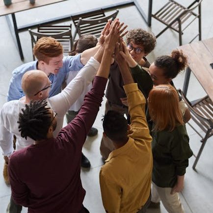 A diverse group of professionals high-fiving in a modern office, showcasing teamwork and collaboration.